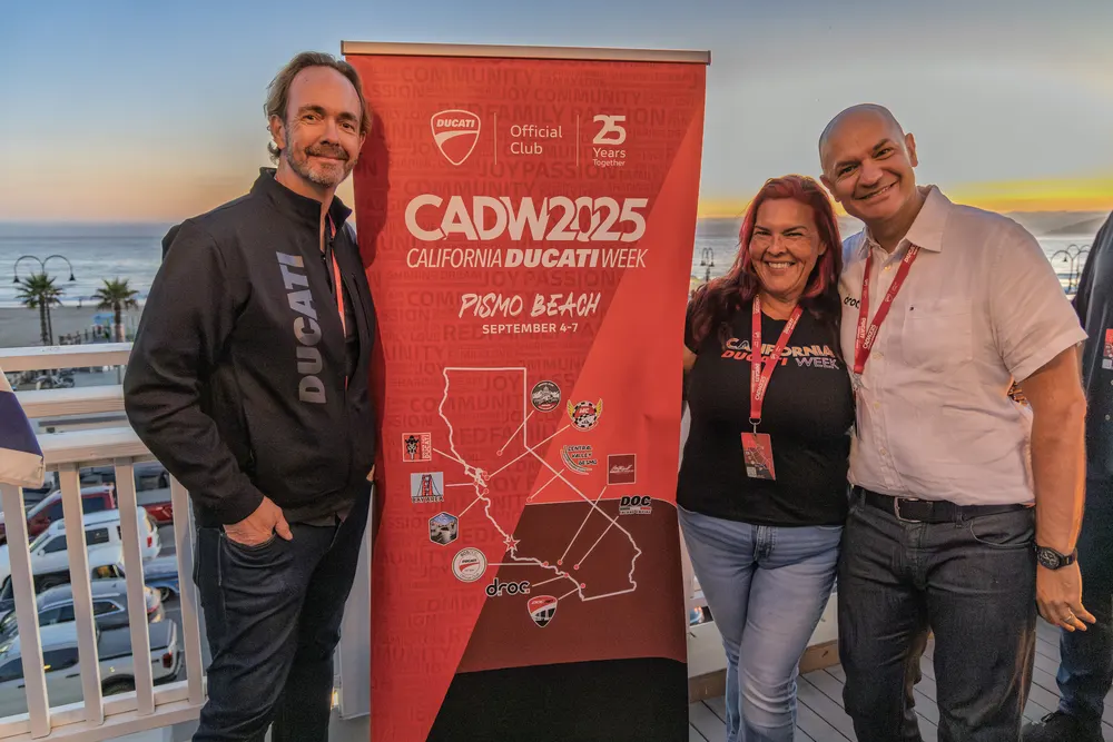Four attendees at the CADW 2025 banner with the ocean and sunset behind them