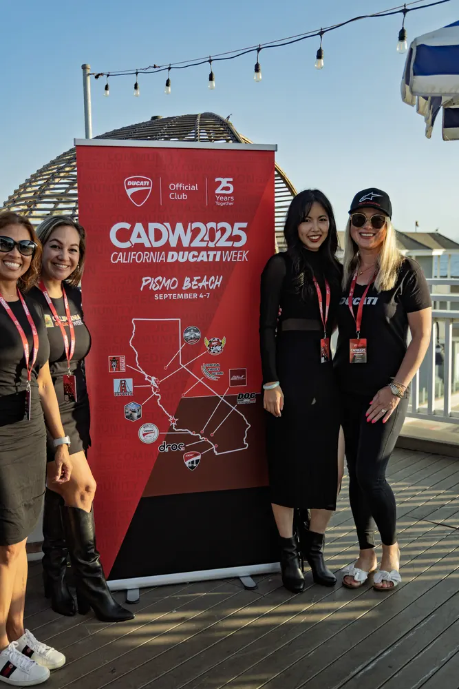 Four attendees at the CADW 2025 banner under string lights on the pier deck