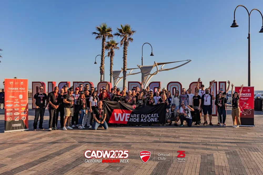 The full CADW 2025 group on the Pismo Beach boardwalk in front of the PISMO BEACH letters, holding a We Are Ducati We Ride As One banner