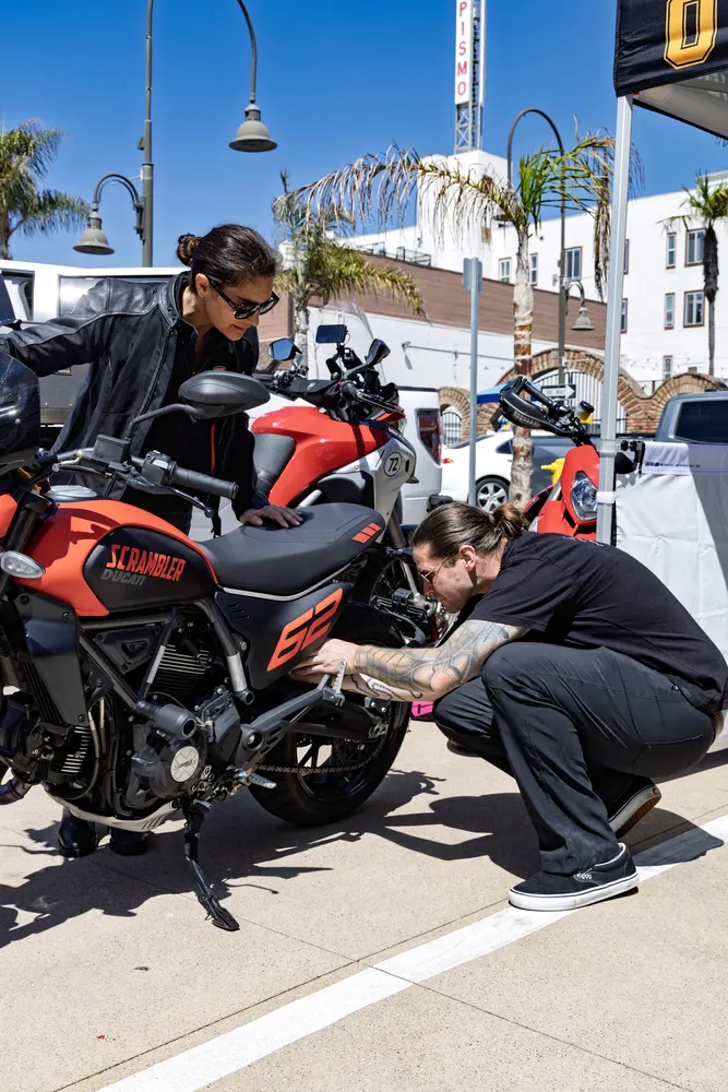 Two attendees looking over a red Ducati Monster at the street display in Pismo Beach
