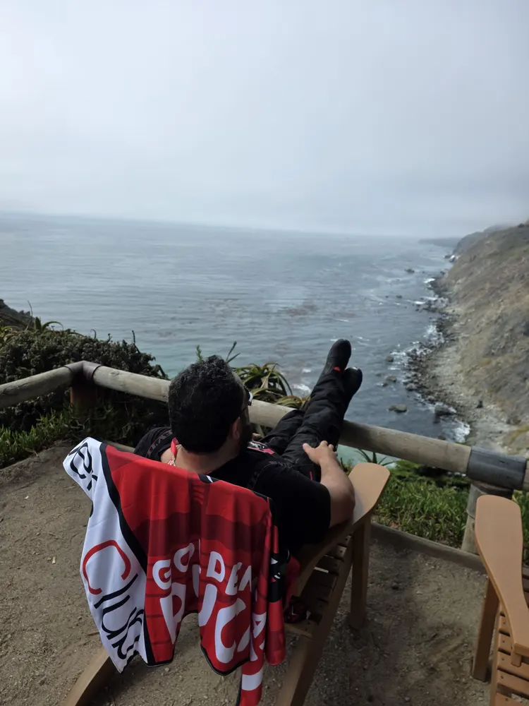 A rider resting with a Ducati Official Club flag above the fog-covered Big Sur coastline