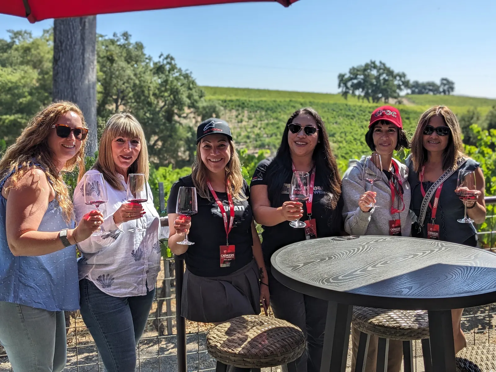 Four CADW participants enjoying wine beneath a red umbrella beside the vines
