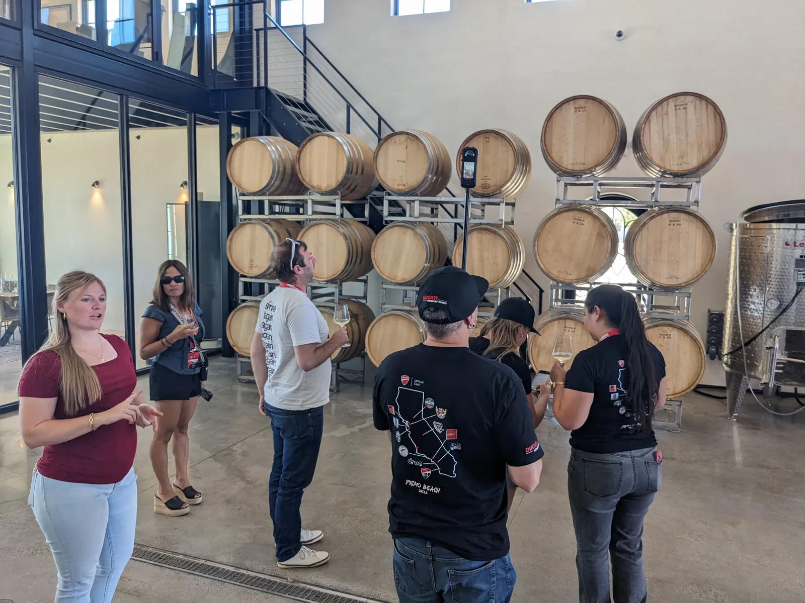 A winery guide speaking to CADW participants beside rows of barrels
