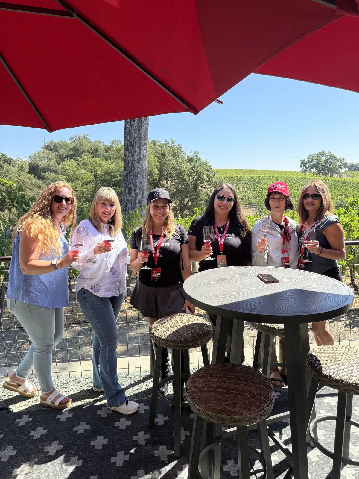 Three friends raising their glasses beneath a red winery umbrella
