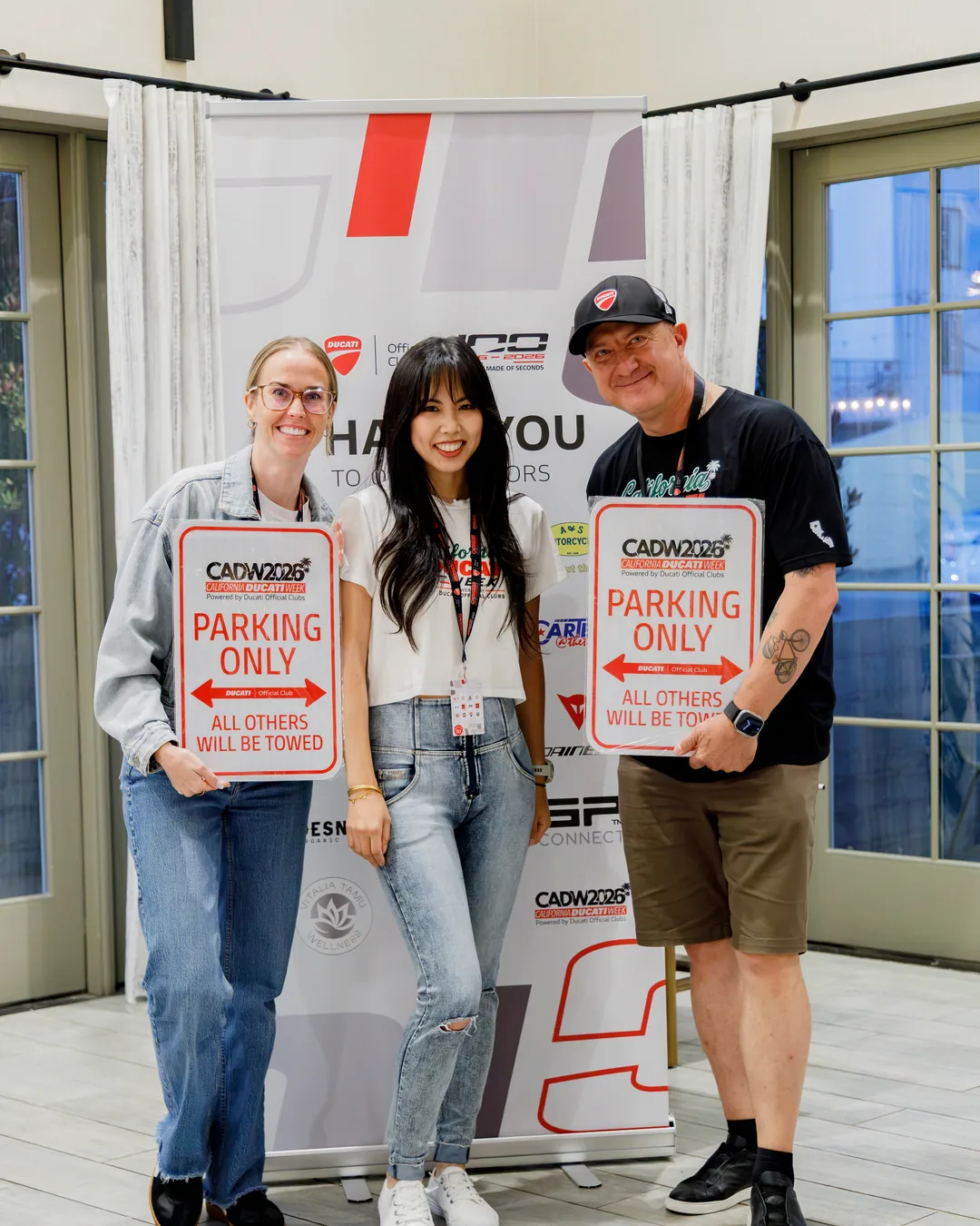 Three attendees holding Ducati parking signs at the Saturday closing ceremony and giveaways.