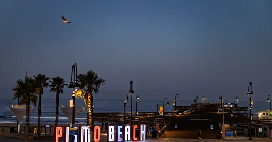 The illuminated Pismo Beach sign and palm trees at dusk.
