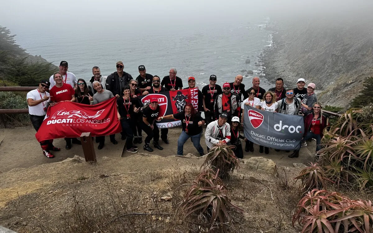 Ducati riders gathered with red Ducati flags on the cliffs at Ragged Point